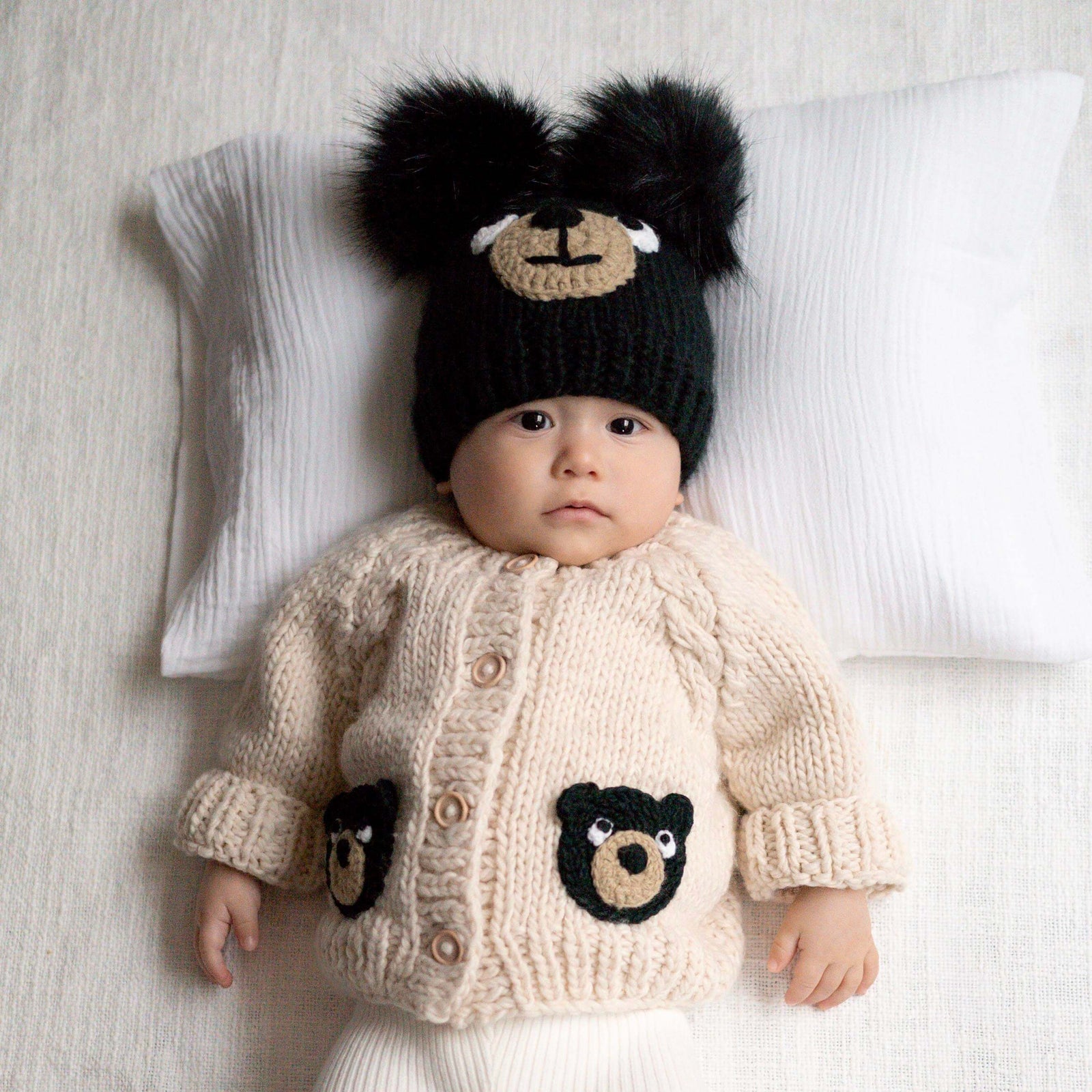 Baby wearing a knitted cardigan and hat with bear designs on a white background